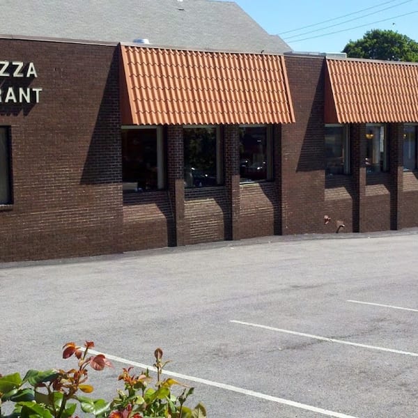 Exterior of Hope Pizza Restaurant, a brick building with orange awnings and a parking lot in front.