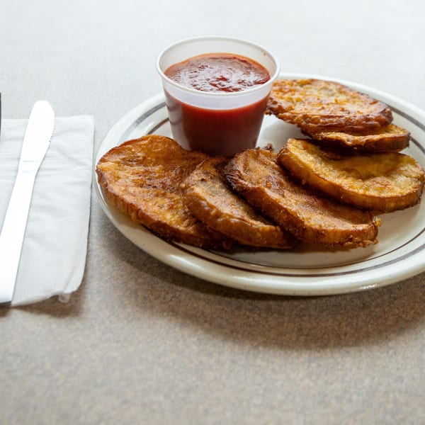 A plate of golden-brown fried plantains with a side of red dipping sauce and silverware.