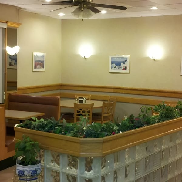 Cozy restaurant interior with booths, tables, wall art, and a planter with greenery.