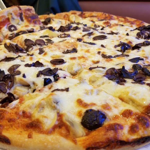Close-up of a whole pizza with white cheese, artichoke hearts, and black olives.