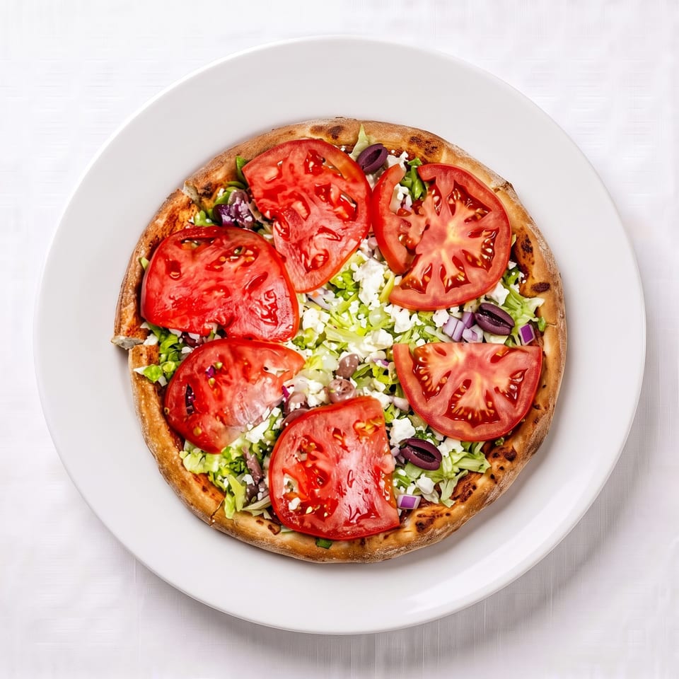 Overhead view of a small pizza topped with sliced tomatoes, lettuce, feta cheese, and olives.