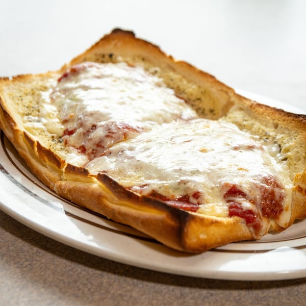A close-up of a cheesy bread with melted mozzarella and red sauce on a white plate.