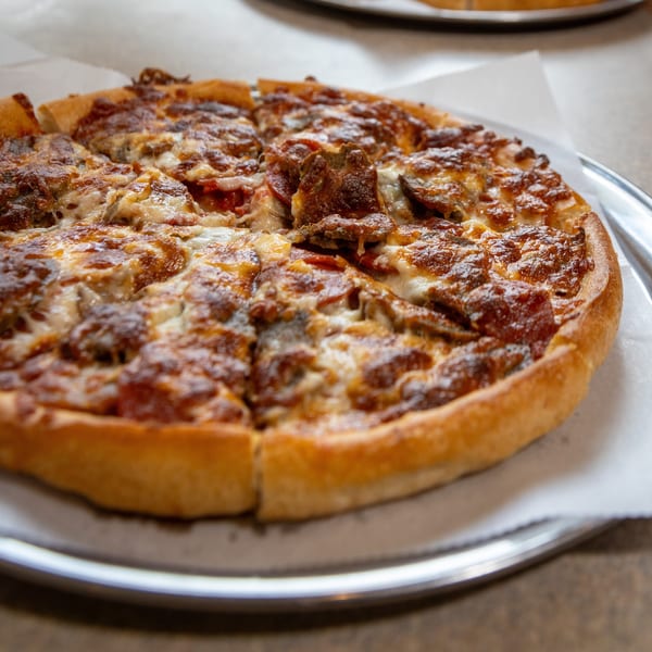 A freshly baked, sliced pizza with pepperoni, sausage, and melted cheese on a metal tray.