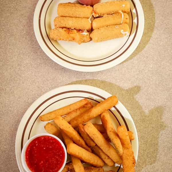 Two plates of fried appetizers, one with mozzarella sticks and the other with fried zucchini, both with marinara sauce.