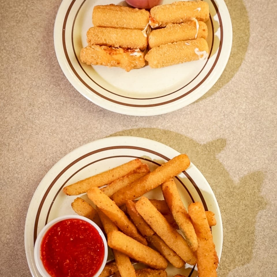 Two plates of fried appetizers, one with mozzarella sticks and the other with fried zucchini, both with marinara sauce.