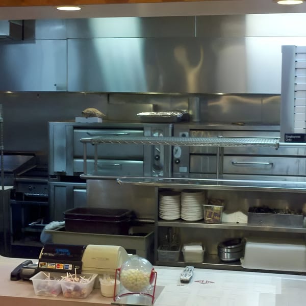 A commercial kitchen with stainless steel appliances, shelves of plates, and a counter with a cash register.