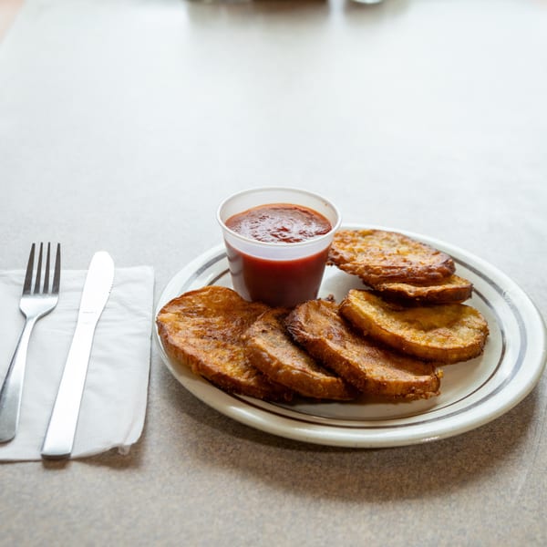 A plate of fried plantains with a side of red sauce, fork, and knife on a table.