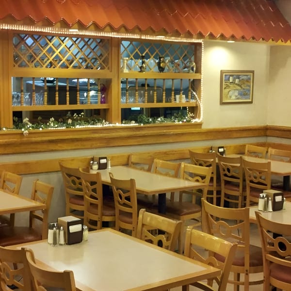 Empty restaurant dining room with light wood tables and chairs, and a decorative wooden lattice window.