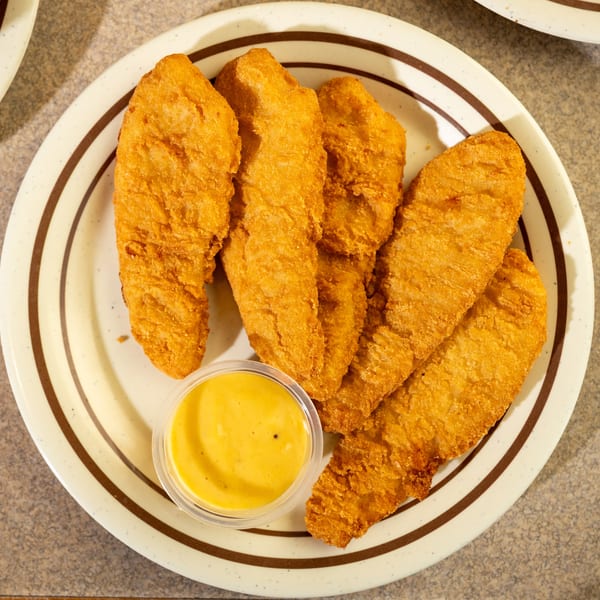Golden-brown fried chicken tenders and a small cup of honey mustard dipping sauce on a white plate.