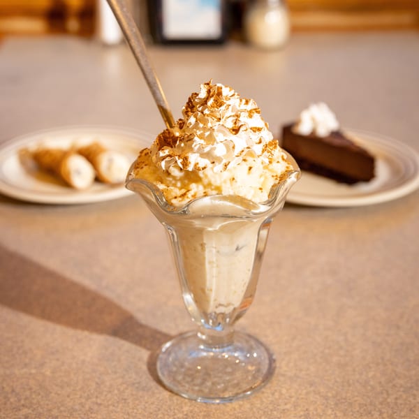 Rice pudding parfait with whipped cream and cinnamon, with cannolis and chocolate cake in the background.